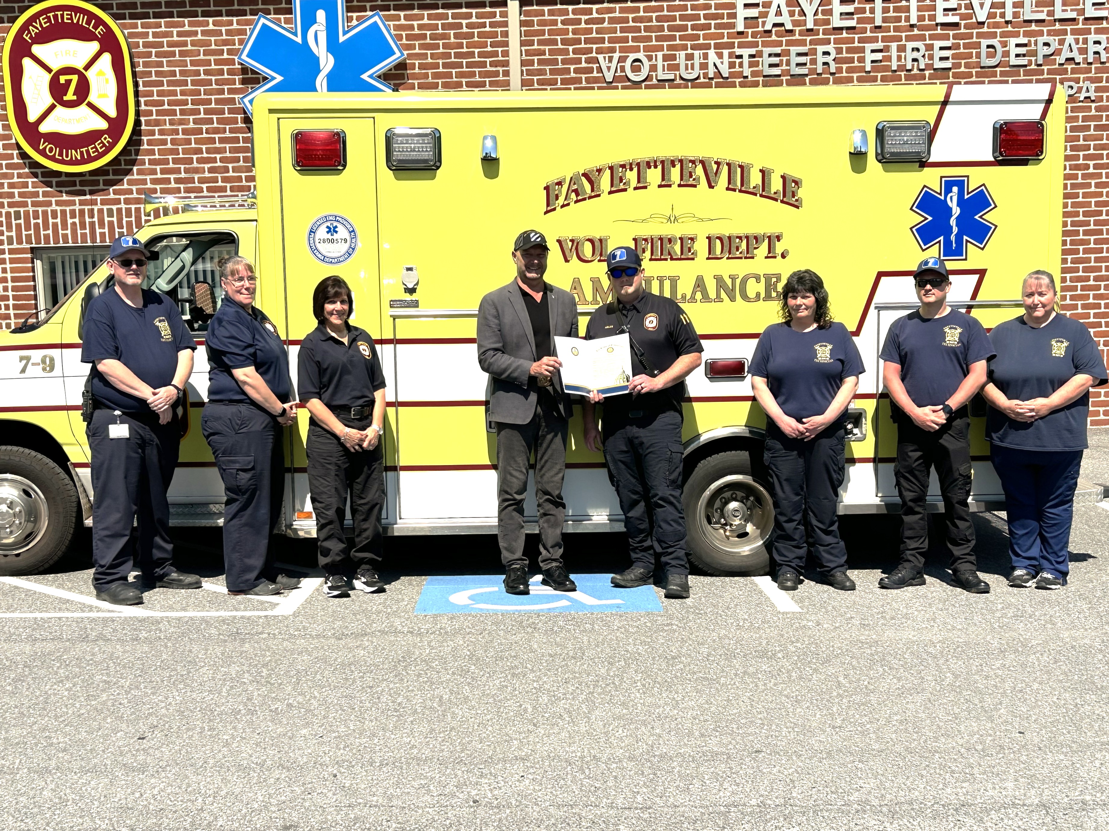 Senator Mastriano standing with several volunteer firefighters in front of a EMS vehicle.