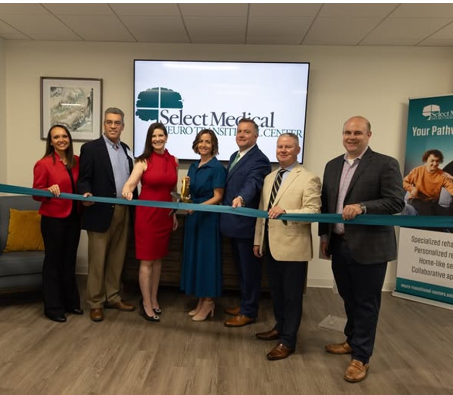 A group of people standing behind a green ribbon before cutting in celebration of Select Medical’s Neuro Transitional Center