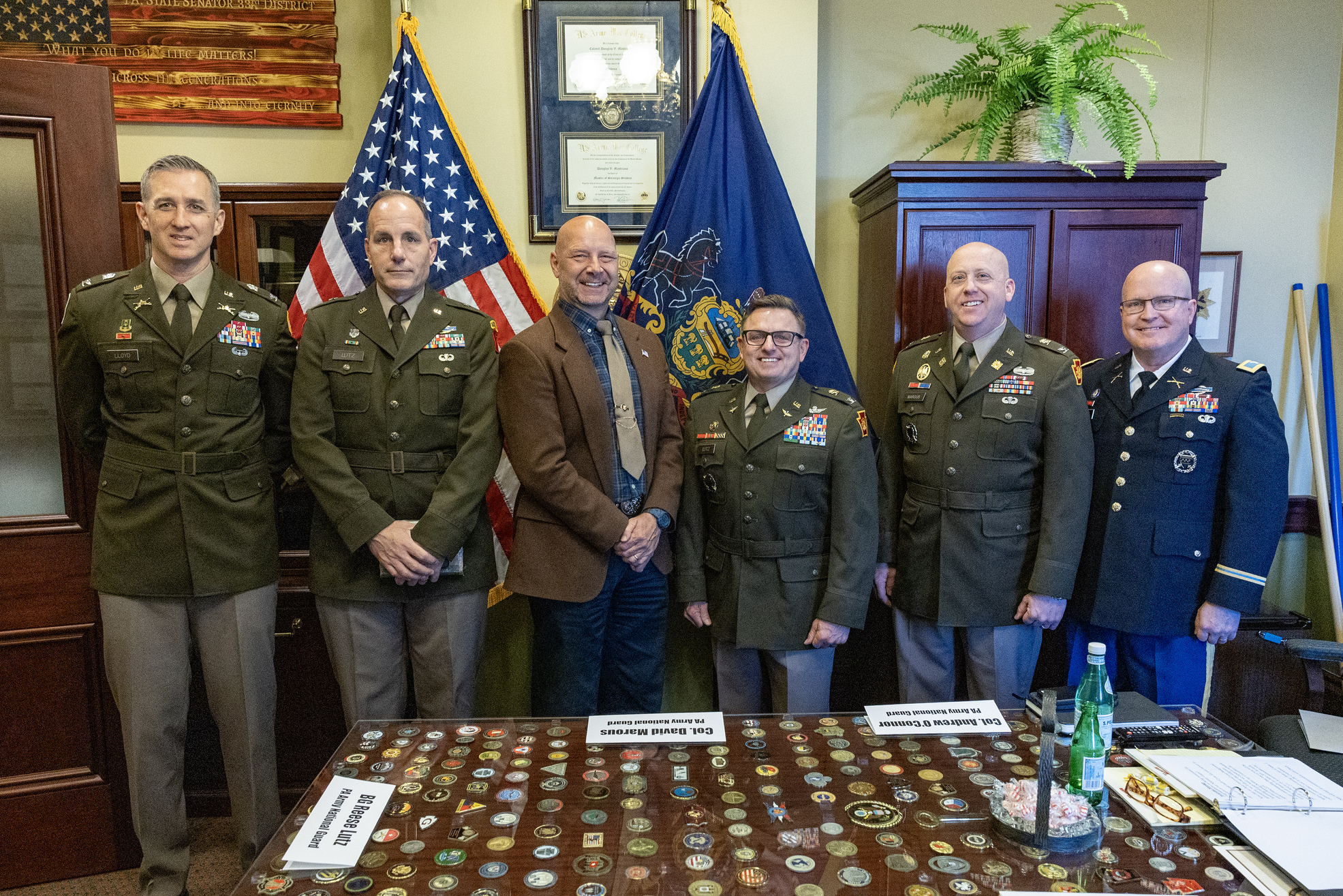 Senator Mastriano in a suit and tie standing in the middle of 5 National Guard Officers in Senator Mastriano’s capitol office in front of the American flag and the PA Senate flag