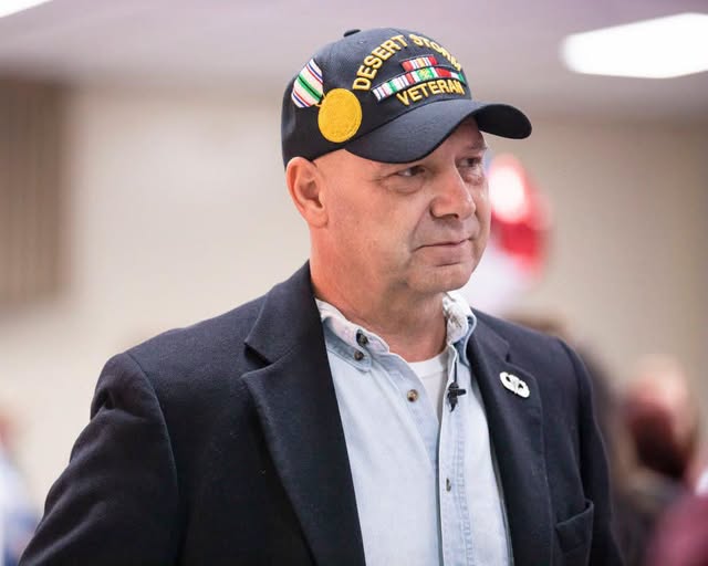 Senator Mastriano in a navy sports jacket, red tie, light blue buttoned down shirt, desert storm veteran hat