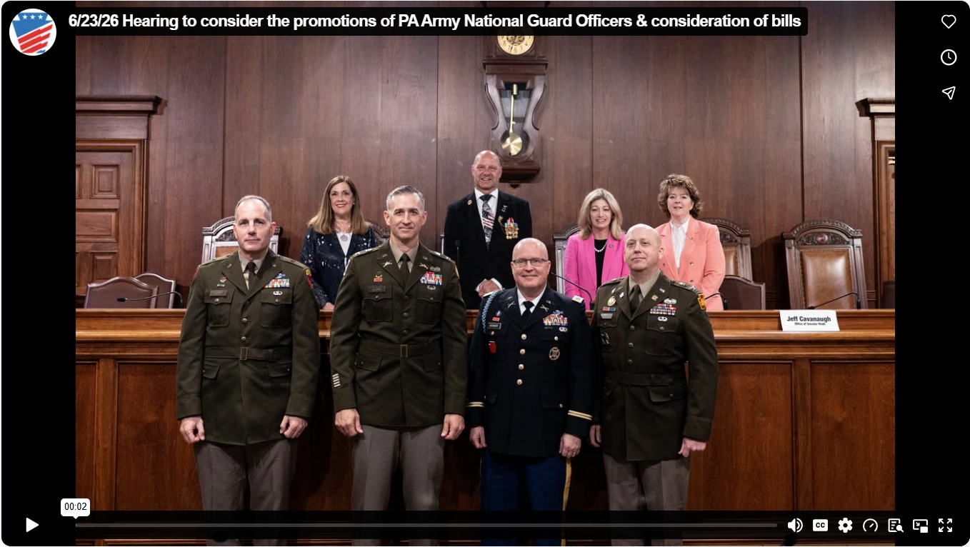 Group photo in a wood paneled hearing room showing Senator Mastriano centered in the back row above a dais, with uniformed military officers standing in front.
