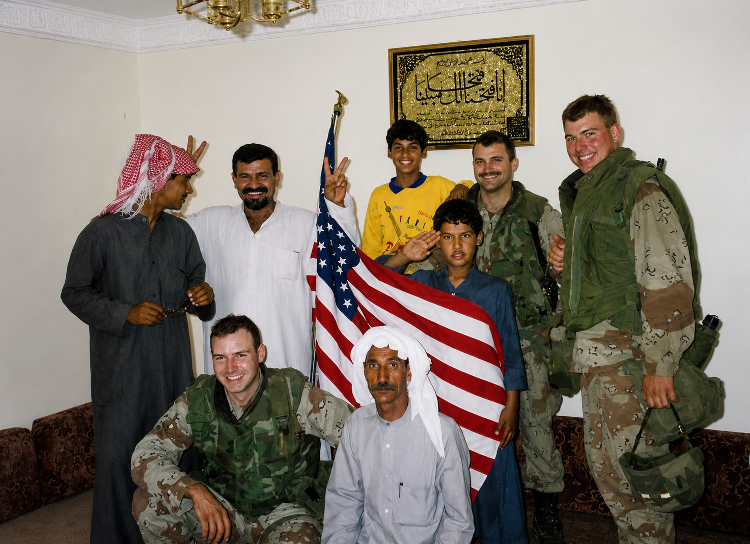 Senator Mastriano in green and beige Army gear kneeling and two of his soldiers standing with a Kuwait family. The American flag is represented in the middle of everyone.