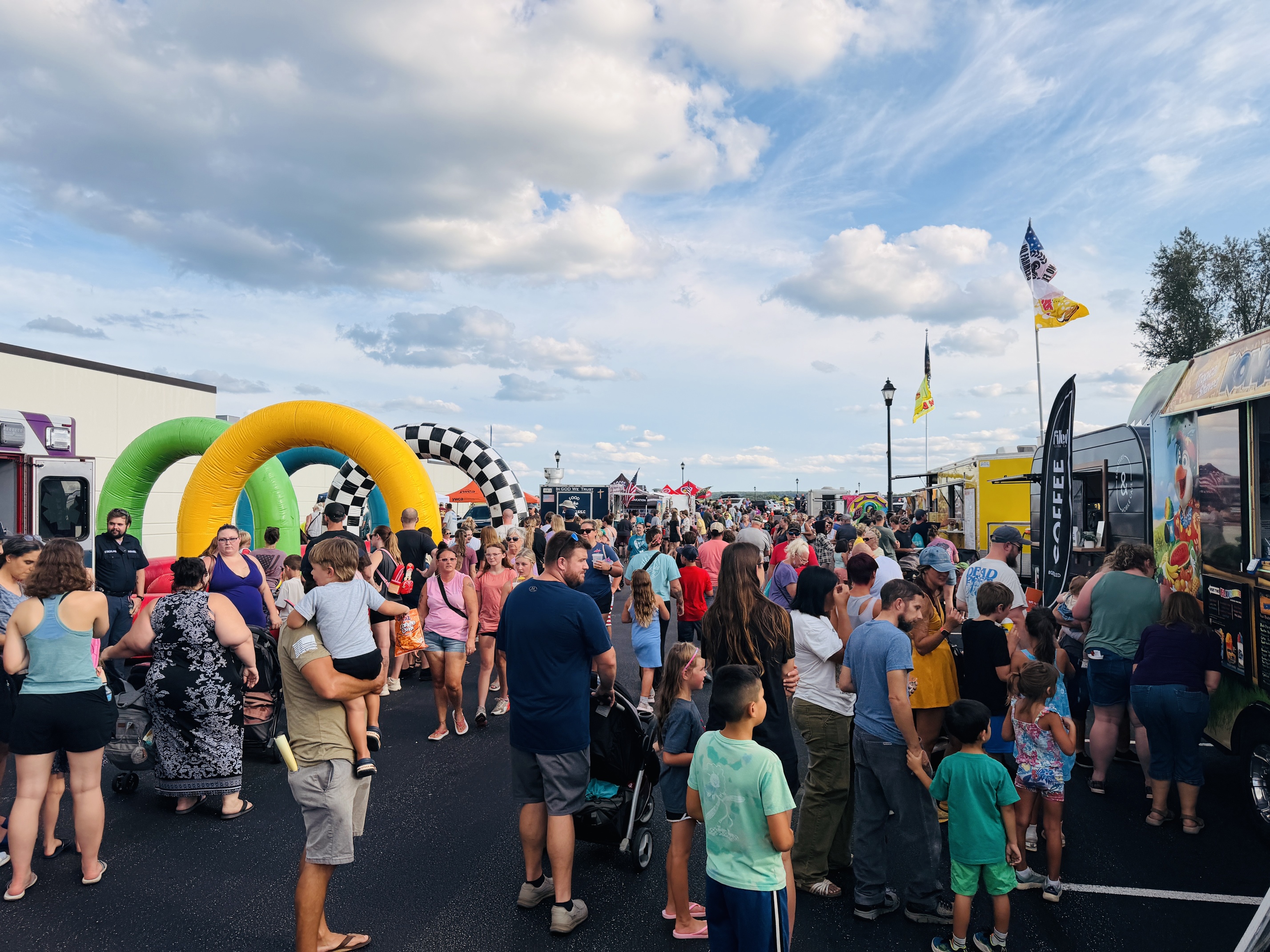 A large crowd of people at an outdoor event with food trucks, vendors, and tents