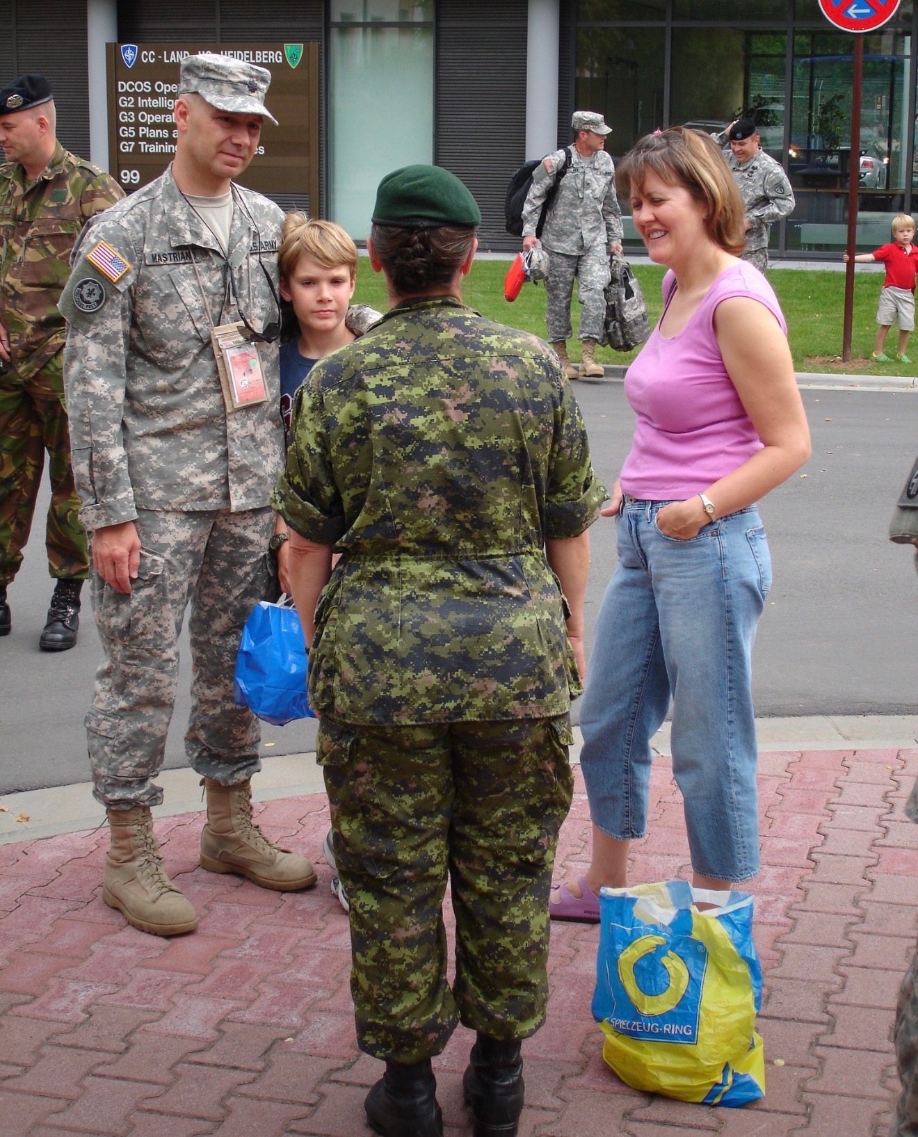 Senator Mastriano in green and brown Army uniform standing next to his son Josiah, his wife Rebbie in a pink tank top, light denim capri jeans, pink Birkenstocks, and a lady dressed in camouflage uniform with her back towards the camera.