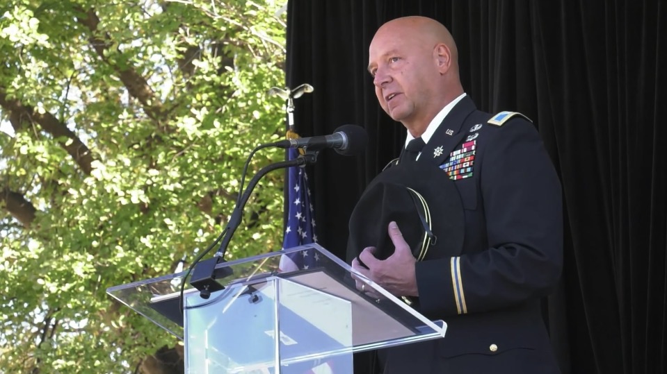 Senator Mastriano in his military dress uniform speaks at a clear podium while holding his cavalry Stetson hat.